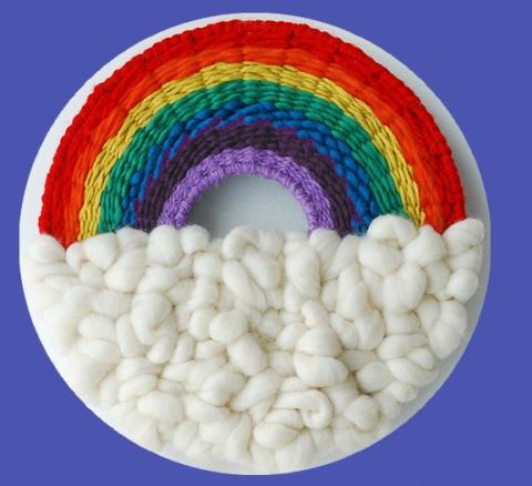 Woven rainbow made of yarn over a cloud of white wool roving.