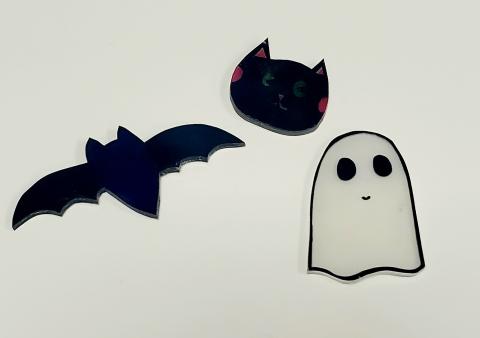 Black bat pin, black cat head pin, and white ghost with black eyes pin on white background