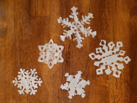 DIY Window Clings. Picture displays 5 white snowflakes of differing designs made with dried glue.