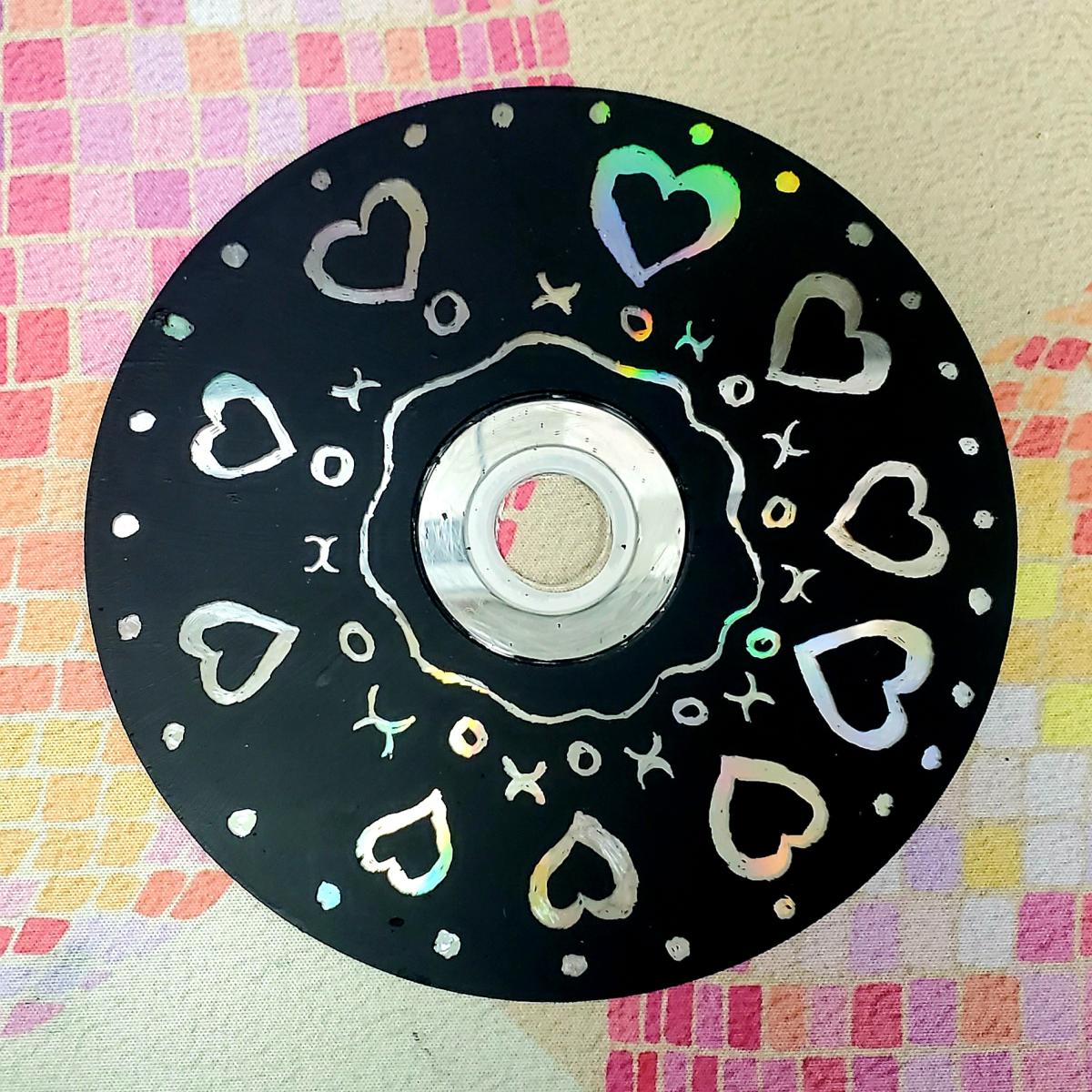 CD painted black with designs etched into paint to create prismatic effect.
