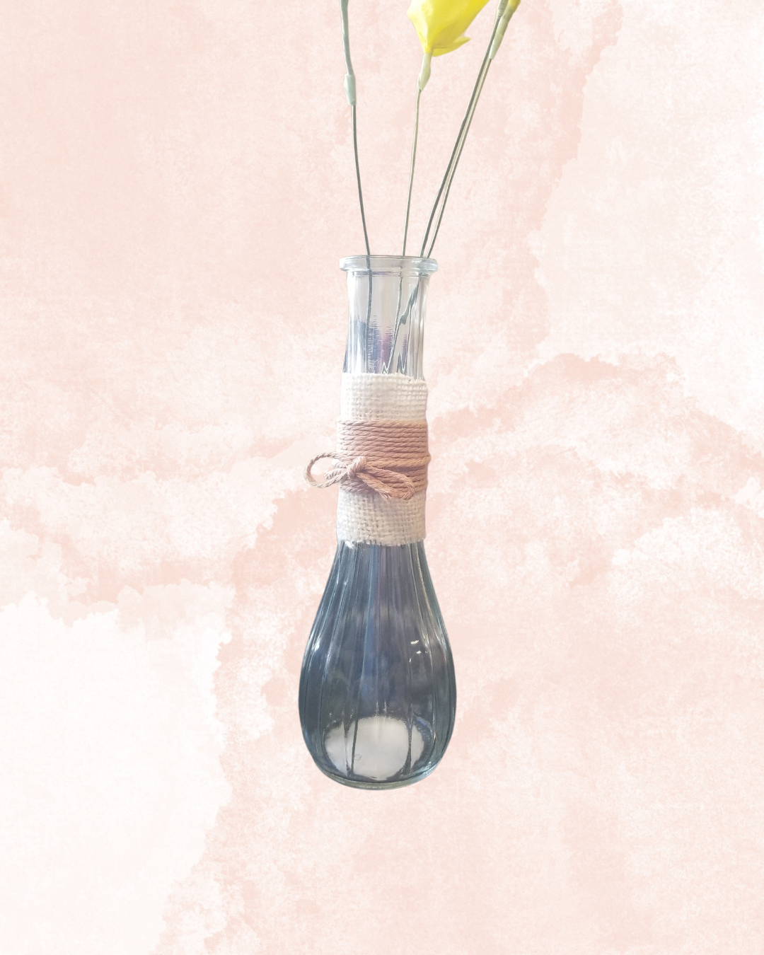 A glass bottle wrapped with a beige burlap piece and then wrapped with twine tied into a bow. 